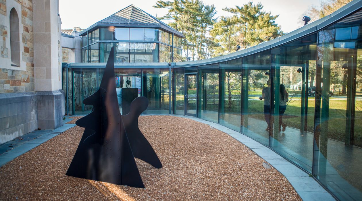 An exterior photo of the Frances Lehman Loeb Art Center at Vassar College in Poughkeepsie, complete with a black metal sculpture and its glass-enclosed walkway.